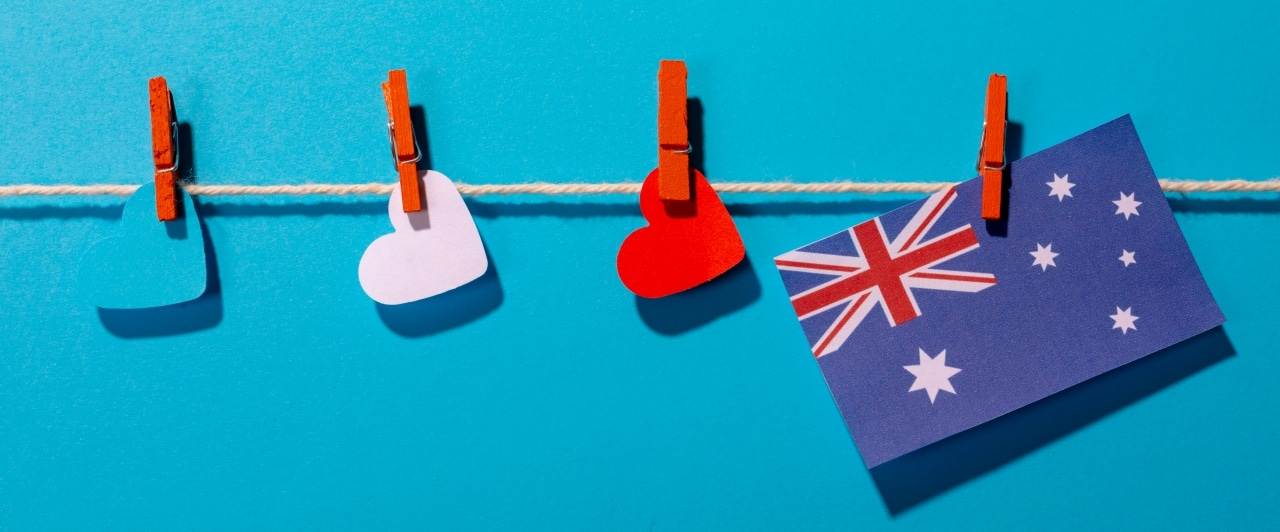 Australia flag with heart shaped papers on clothesline over blue background with copy space. independence day, love and patriotism.