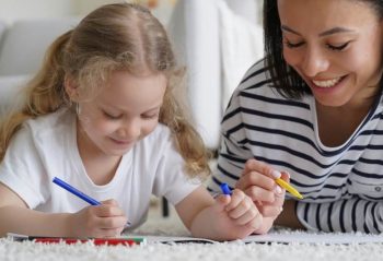 Happy mom, adopted daughter drawing together, lying on floor. Adoption, children's creative leisure
